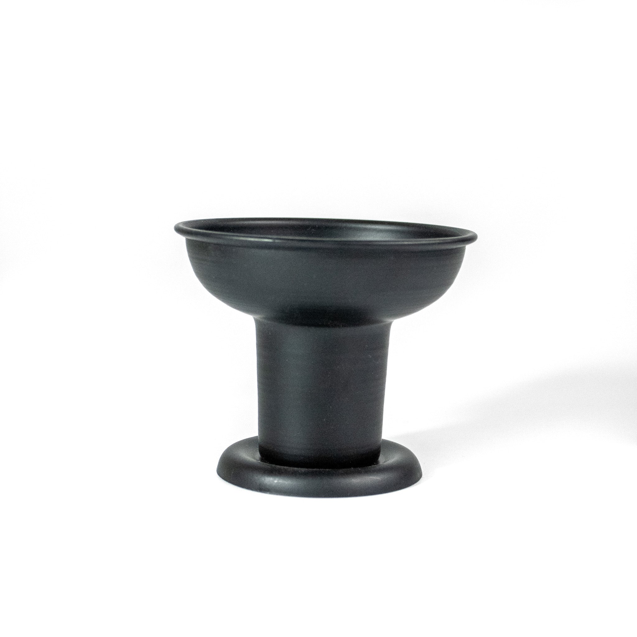 Black pillar candle holder looking at it from the front. It has a narrow base and wider top. 