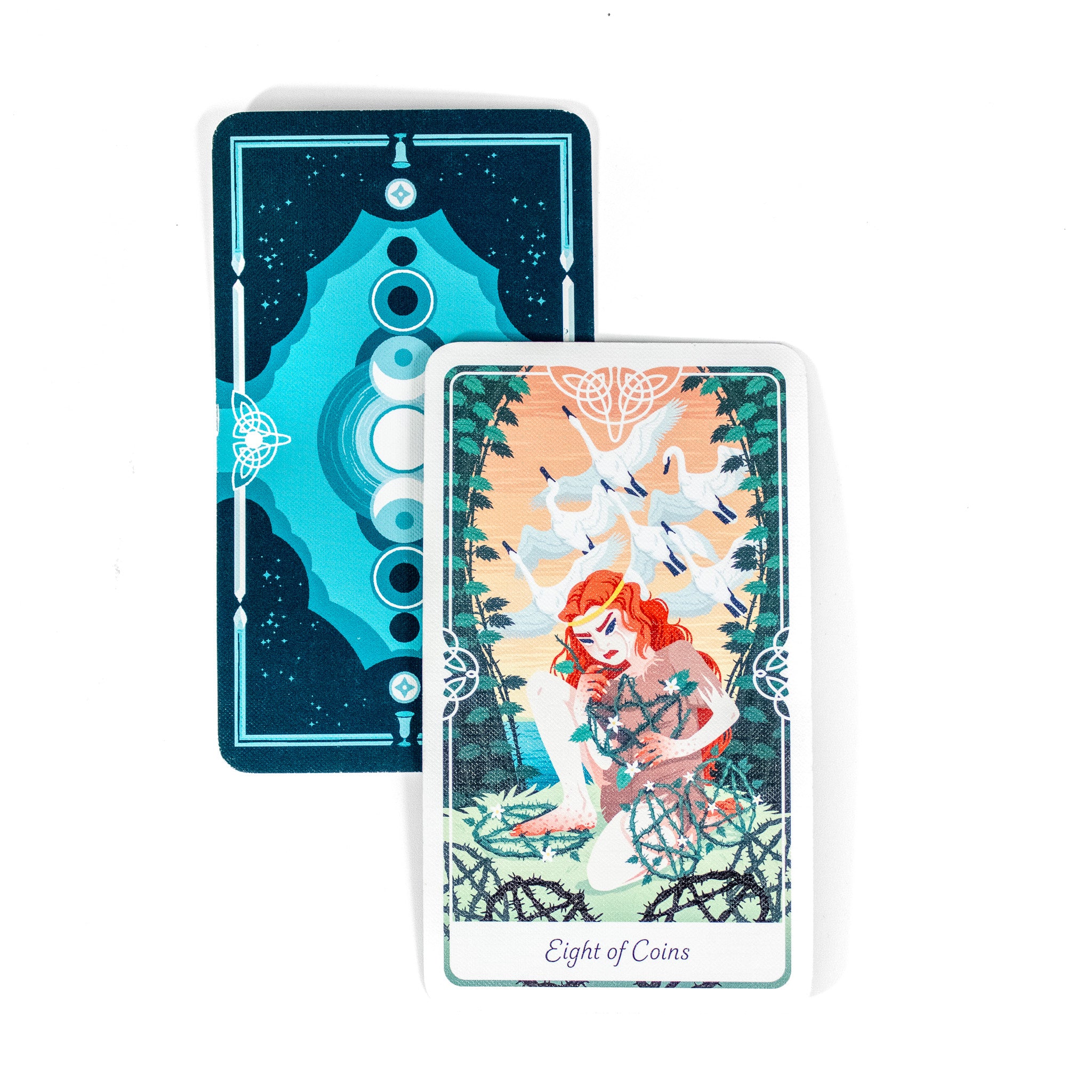 The Eight of Coins card from the Tarot of the Divine shows a woman with red hair creating pentacles. There are geese flying behind her. A second card behind it shows the back of the cards, dark blue with light blue phases of the moon. 