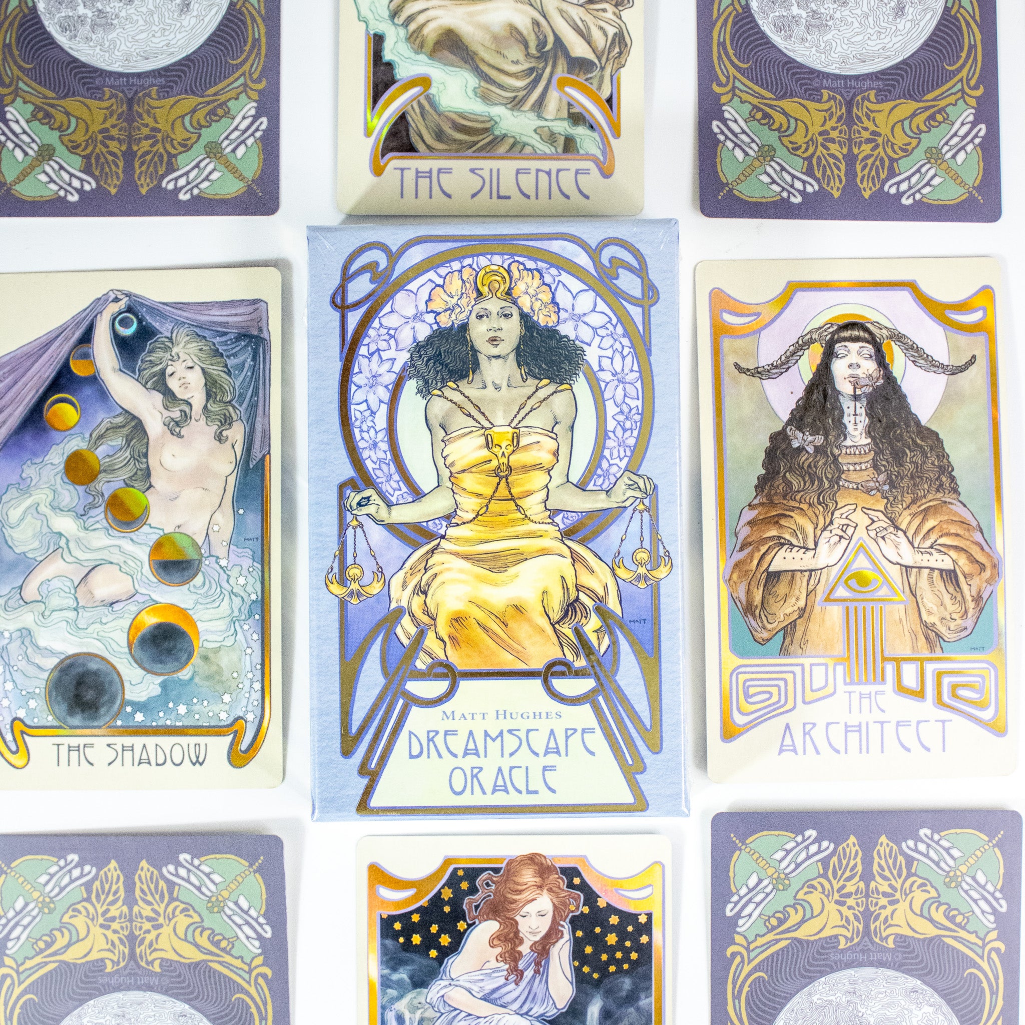 The Dreamscape Oracle deck box is in the center. It shows a Black woman in a thrne, wearing a golden dress and holding the scales of justice. She wears a flower crone. Other cards from the deck are around it