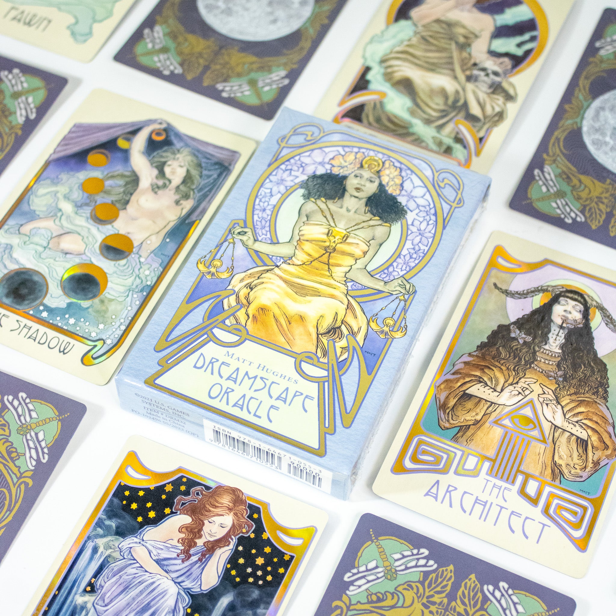 The Dreamscape Oracle deck box is in the center. It shows a Black woman in a thrne, wearing a golden dress and holding the scales of justice. She wears a flower crone. Other cards from the deck are around it