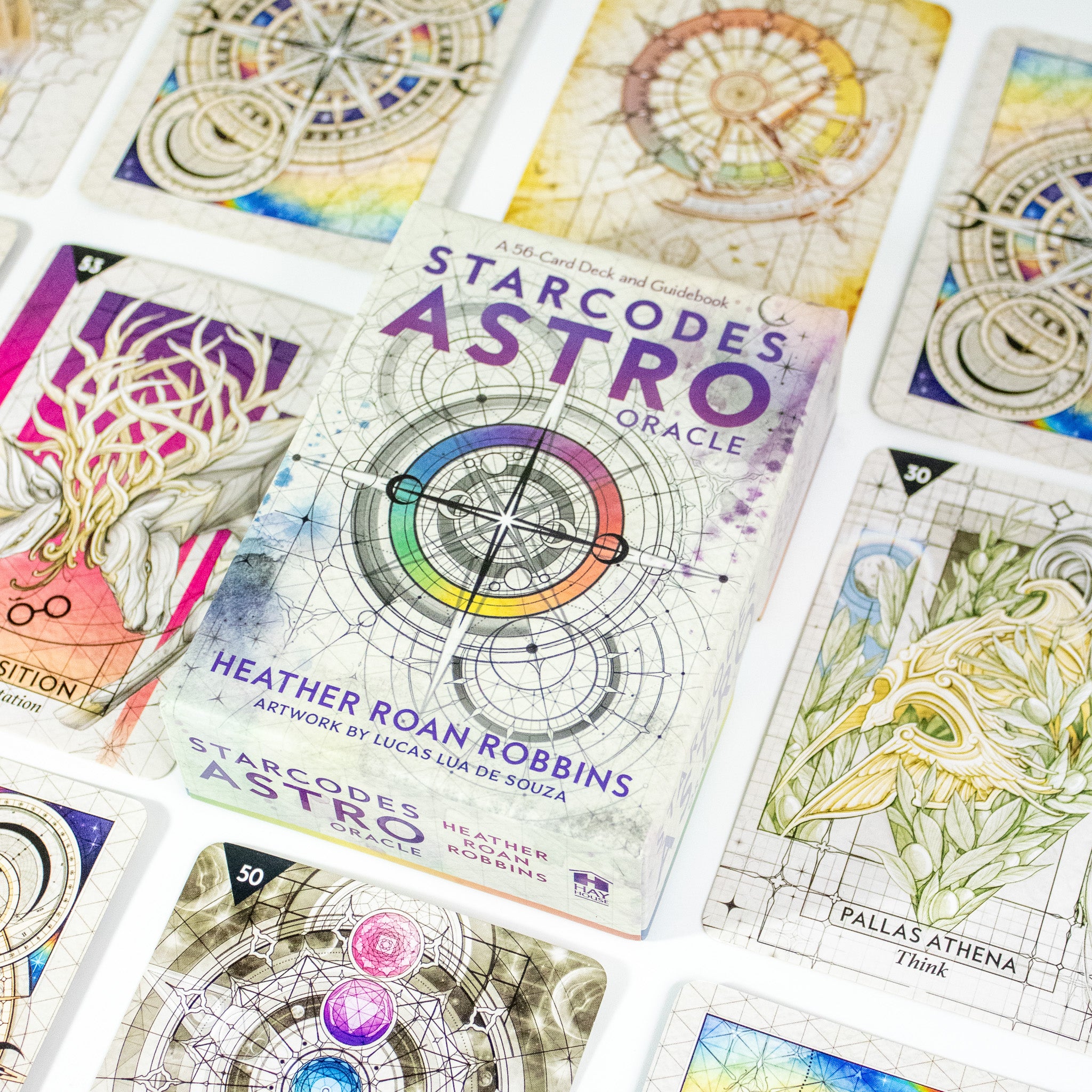 Starcodes Astro Oracle deck box. Has a compass in the center with rainbow band around it and other sacred geometry. Other cards from the deck surround the box