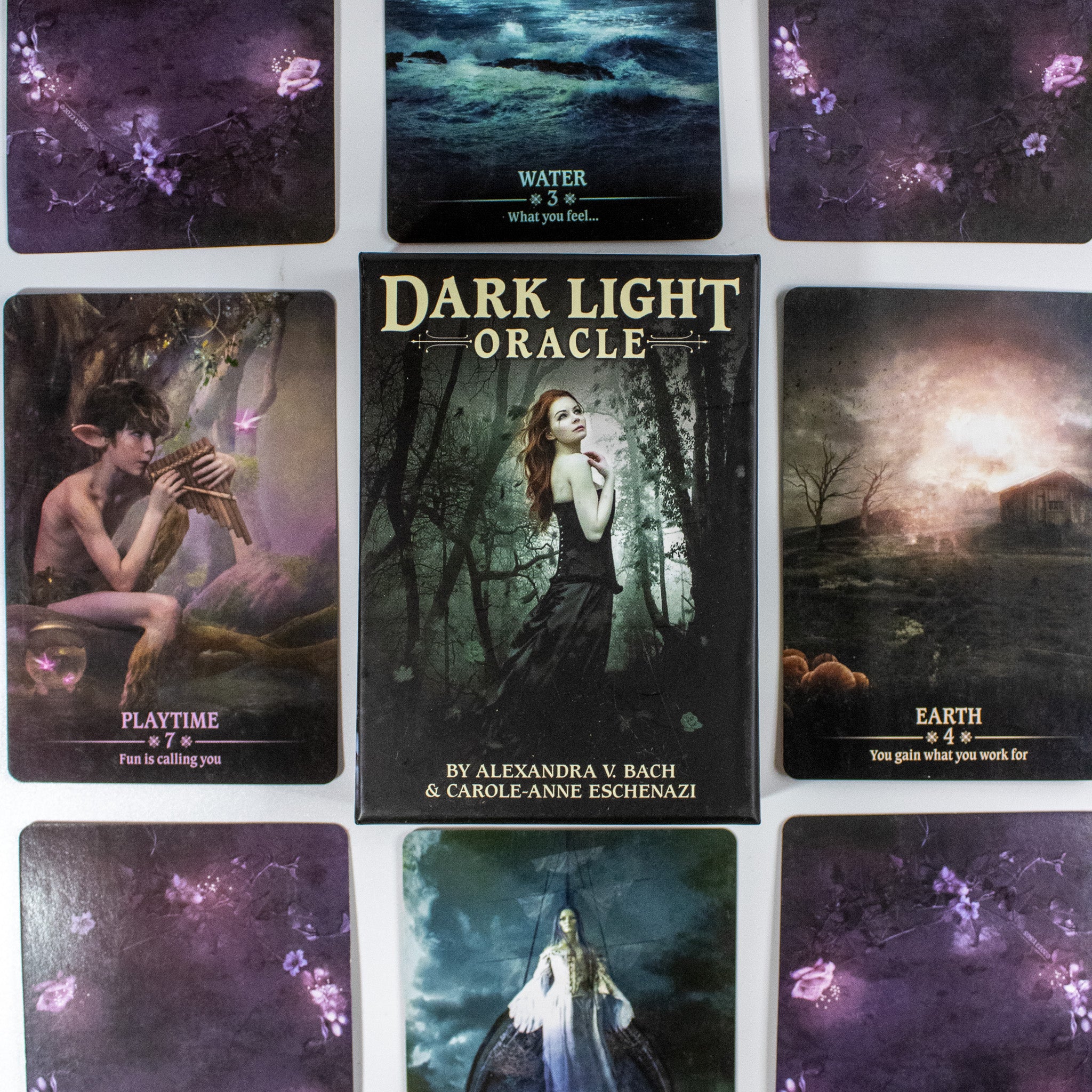 Box of Dark Light Oracle deck in the center with a woman with red hair in a black dress in a dark forest. Other oracle cards surround it.