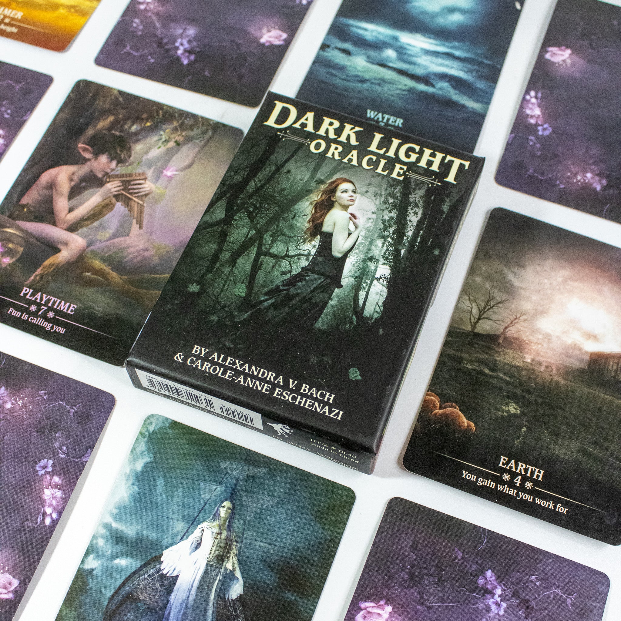 Box of Dark Light Oracle deck in the center with a woman with red hair in a black dress in a dark forest. Other oracle cards surround it. 