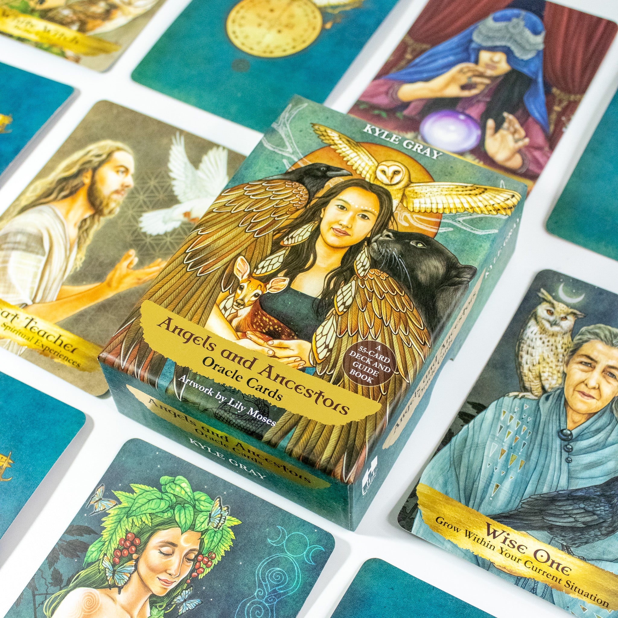 Angels and Ancestors Oracle by Kyle Gray deck box surrounded by cards from the deck. Box has a photo of a Native woman with an owl above her, surrounded by a raven, cougar and holding a fawn. She is winged. 