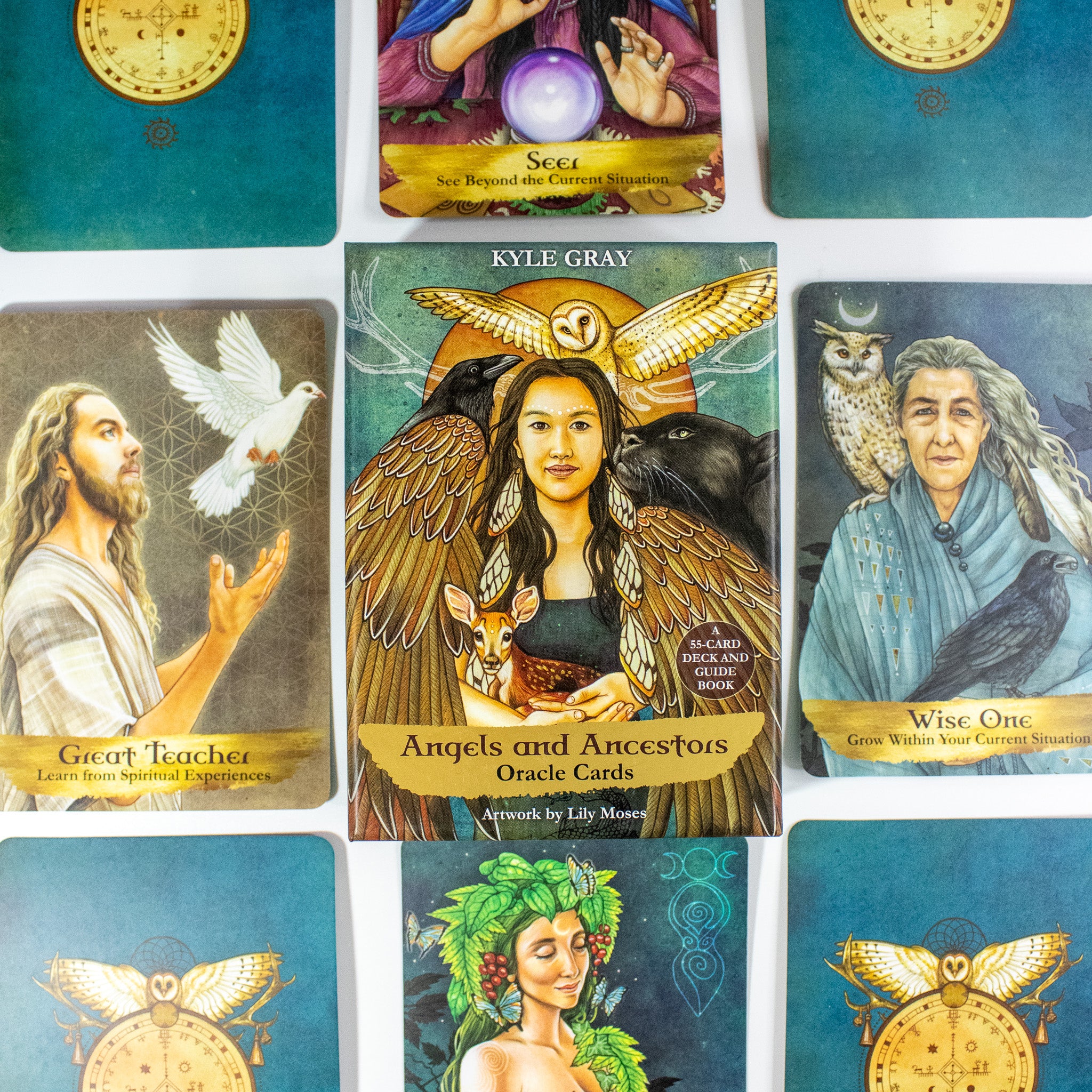 Angels and Ancestors Oracle by Kyle Gray  deck box surrounded by cards from the deck. Box has a photo of a Native woman with an owl above her, surrounded by a raven, cougar and holding a fawn. She is winged.
