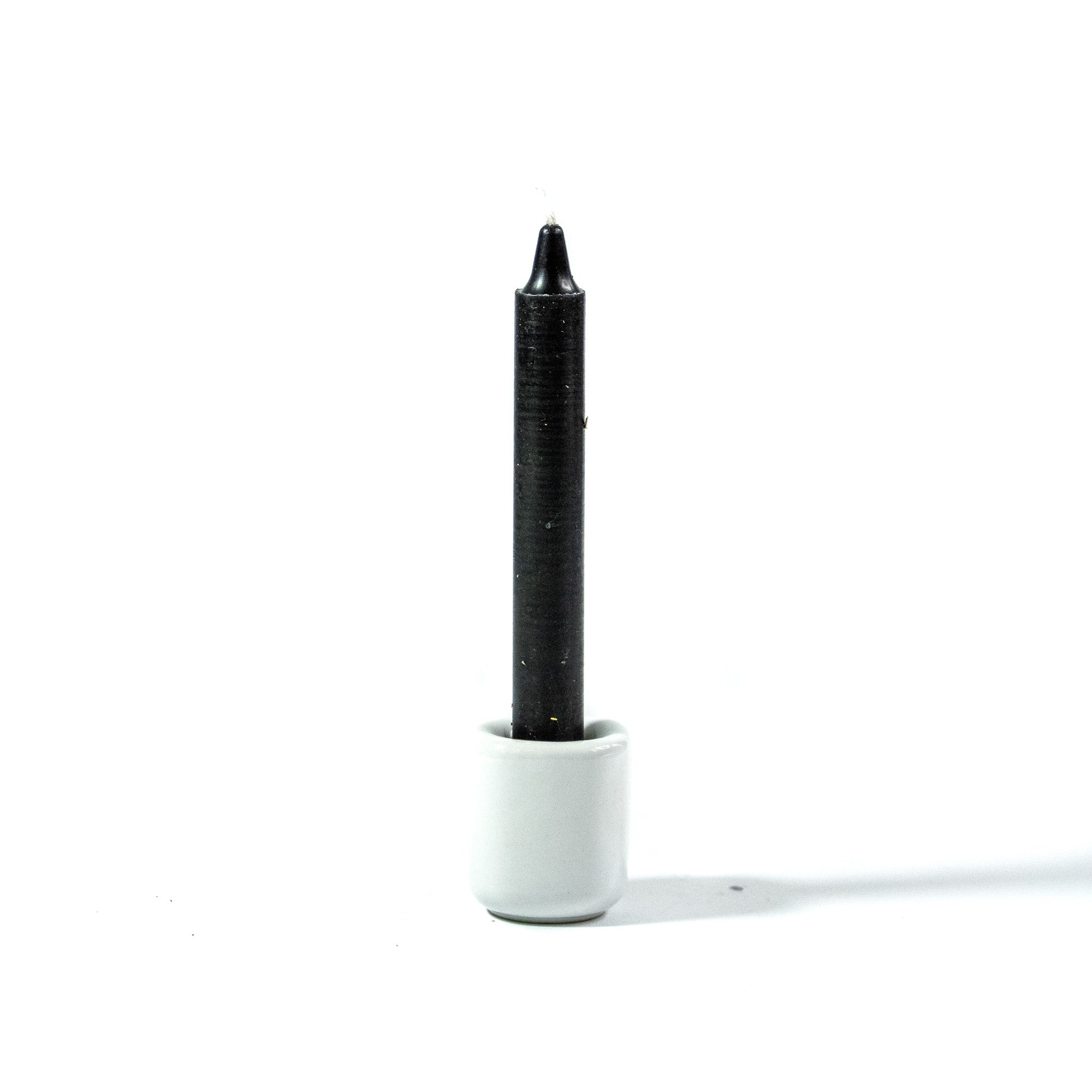 Black chime candle for spellwork and intention setting, set in a white ceramic candle holder with white background.