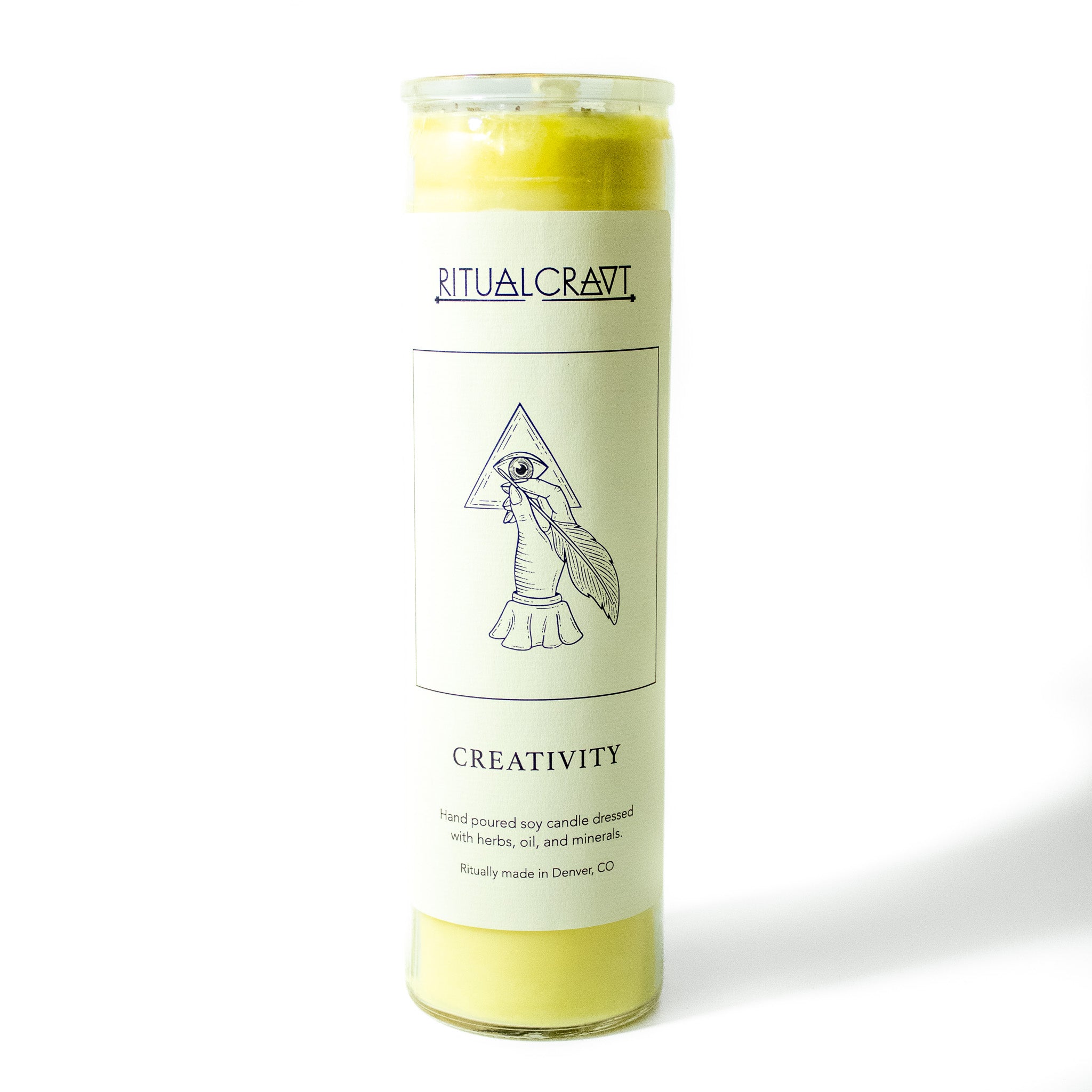 Yellow 7 day jar ritual candle. Label is white with a drawing of a hand drawing an eye inside of a triangle with a feather pen, label says Creativity.