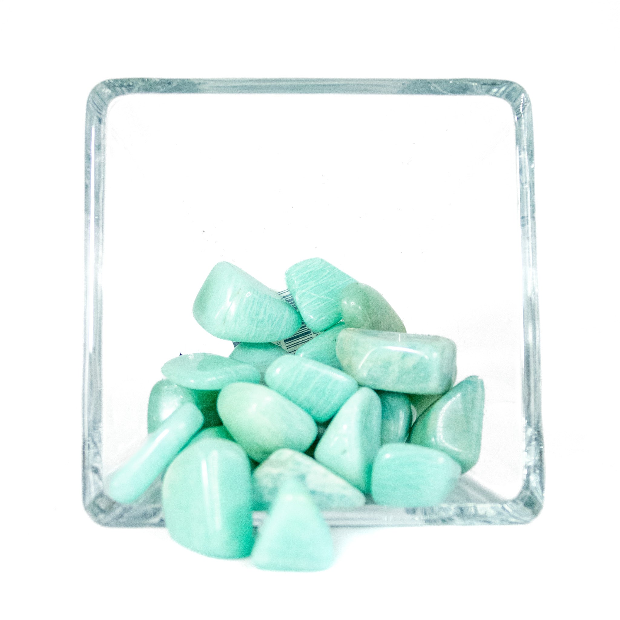 Fifteen tumbled aqua colored Amazonite tumbled pocket stones in a glass bowl with white background. 