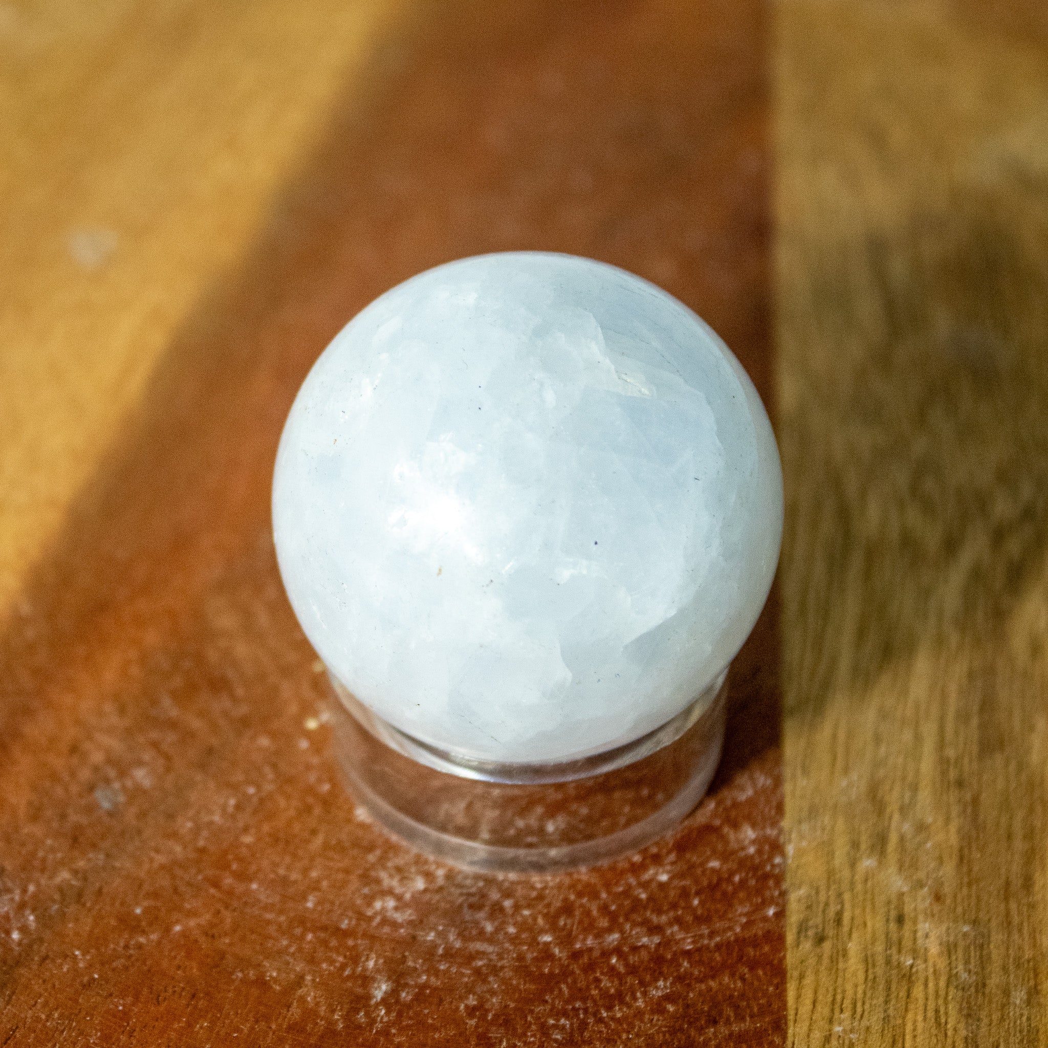 Small blue calcite sphere, very light blue on a plastic sphere holder against a wooden background.