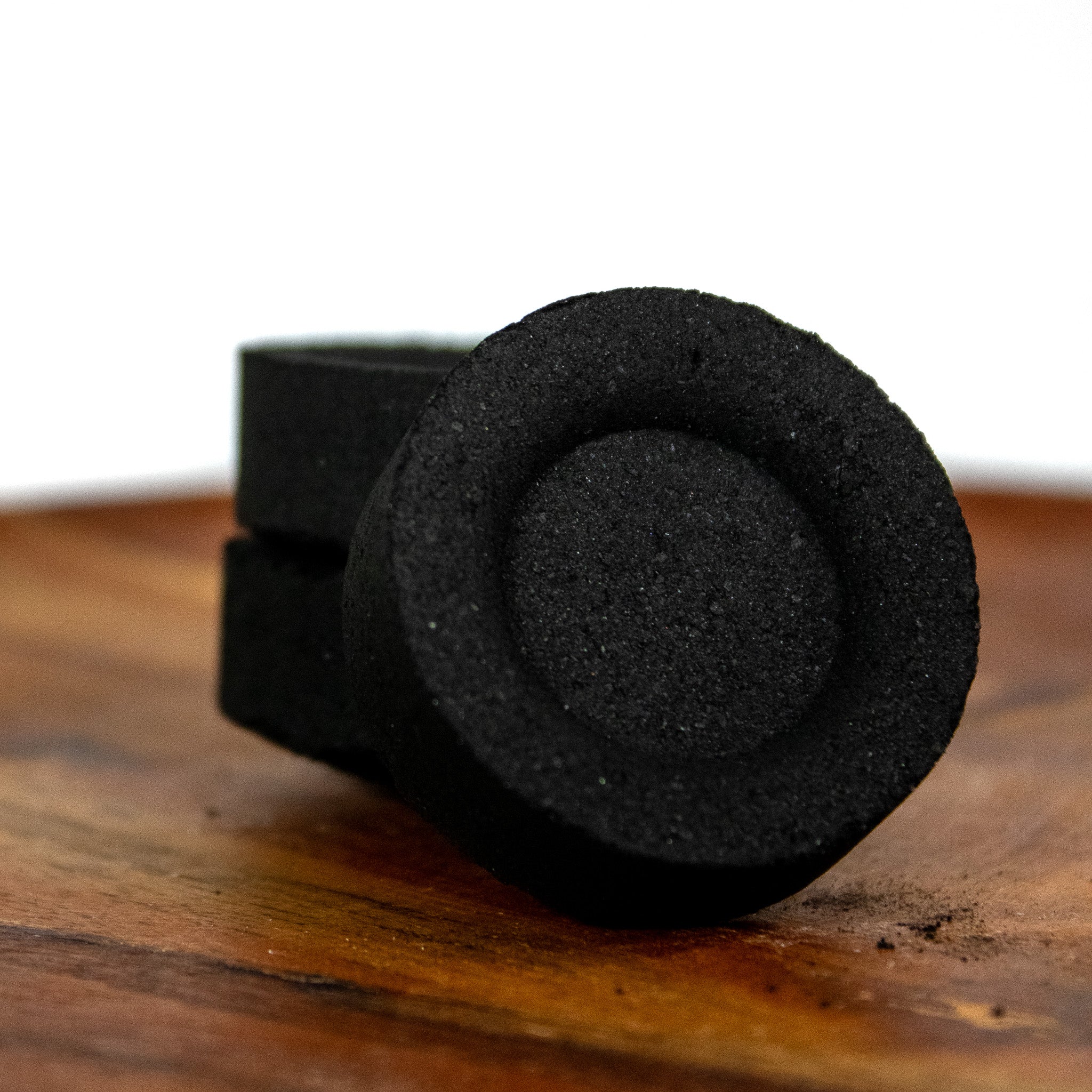 Close up of three charcoal briquettes leaning against each other on a wooden plate. 