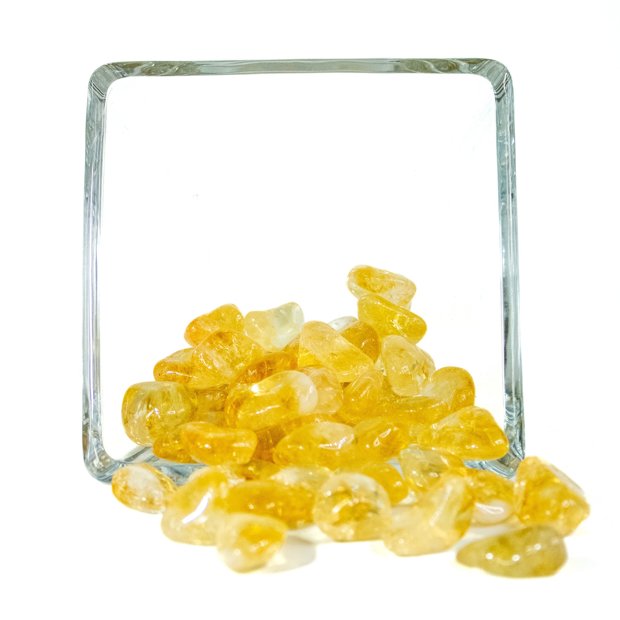 A handful of golden yellow citrine tumbled pocket stones in a glass bowl with white background.