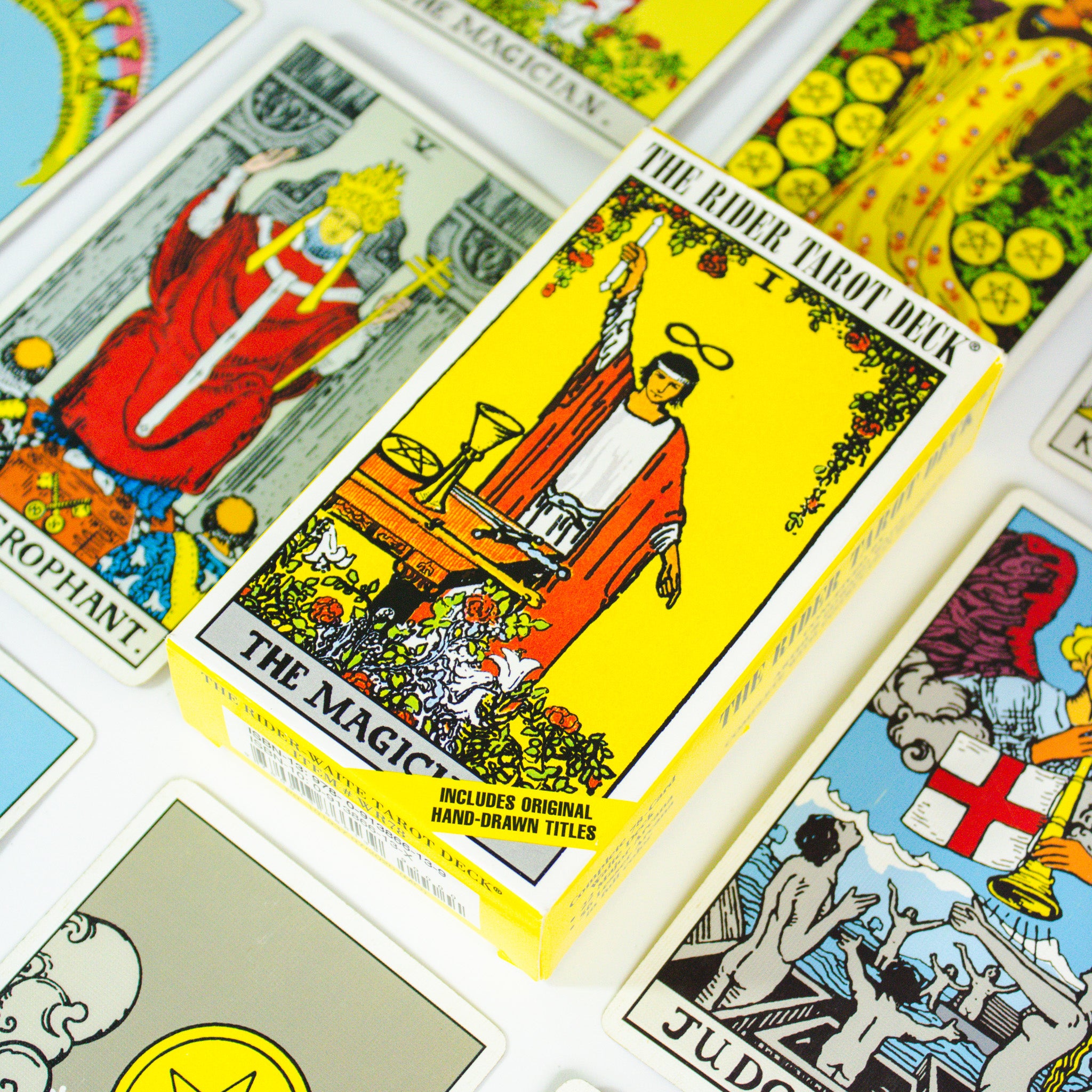 Classic Rider Waite Tarot deck box is yellow with the Magician card image on the front- a man in a red robe holding a wand above his hed. There are several other cards from the deck surrounding the box.