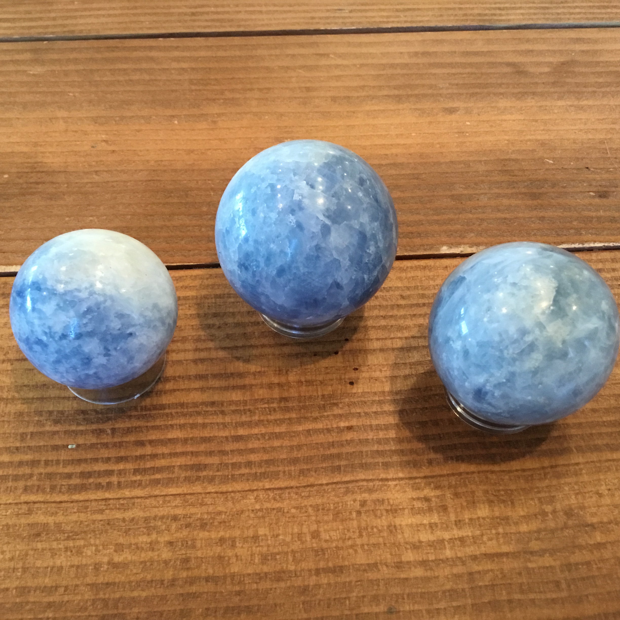 Three blue calcite spheres in varying shades of light blue against a wooden background.