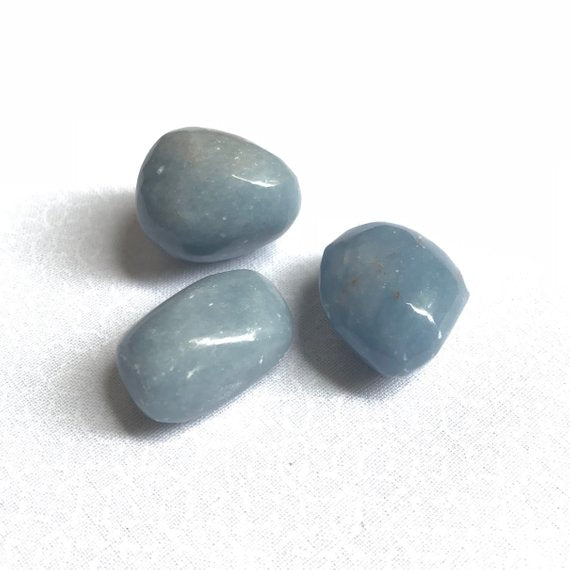 Close up of three light blue angelite tumbled pocket stones. 
